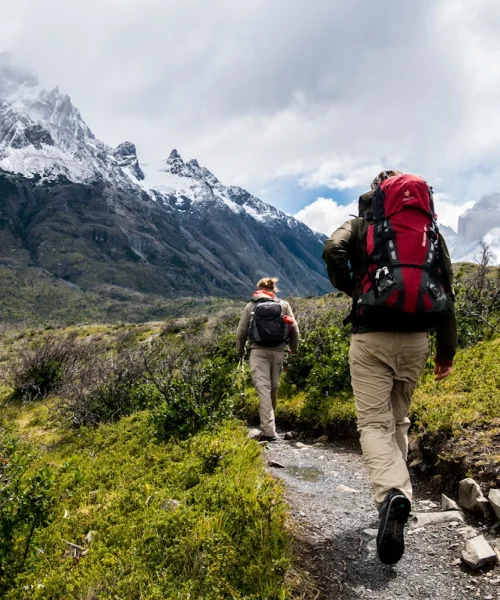 Dos excursionistas con mochilas de montaña caminando por un sendero en la naturaleza.